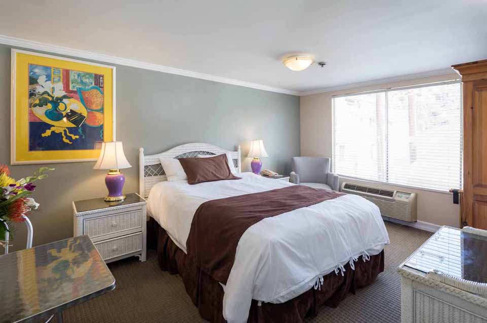 Hotel bedroom with white bedding, brown bed runner, two purple lamps, and a colorful wall art
